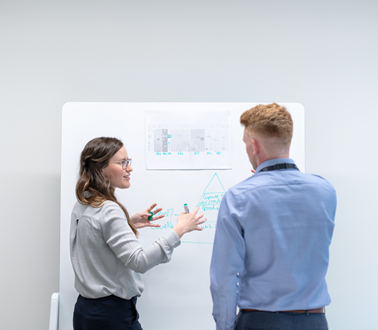 Two engineers discuss work at a whiteboard